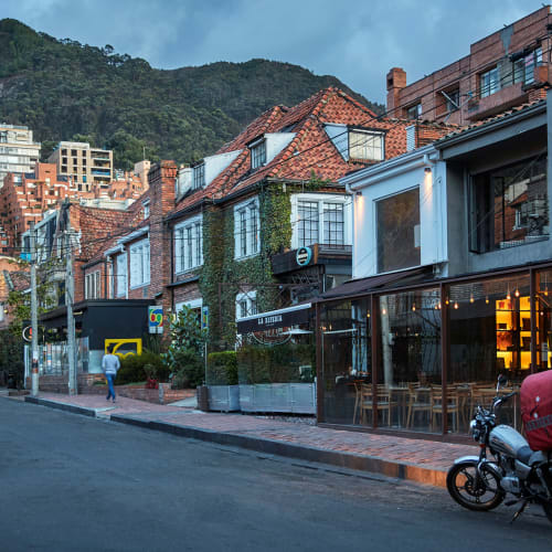 Eine Straßenszene in Bogotá mit bunten Häusern, einige mit Ziegeldächern, und einem Berg im Hintergrund, am Tag.