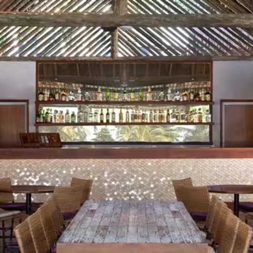 Moderner Tiki-Stil Bar mit Strohdach, Holztischen und Korbsesseln in tropischem Resort-Ambiente.