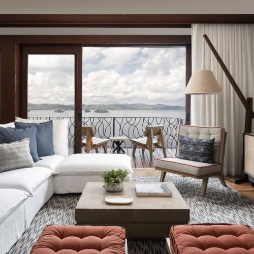 Luxurious lounge area with a large white sectional, armchair, and view of the ocean through sliding glass doors.