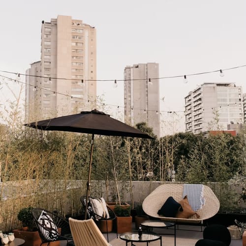 Dachterrasse mit moderner Sitzgruppe, Sonnenschirm und Lichterketten vor einer Kulisse aus hohen Wohngebäuden und vegetation.