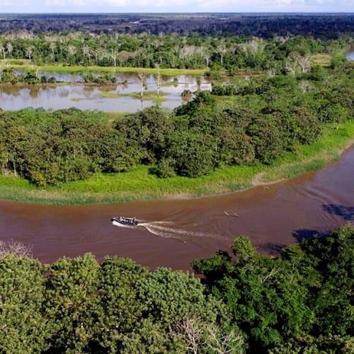 Ein Boot fährt auf dem Amazonas, umgeben von dichtem grünen Wald und kleinen Seen im Hintergrund.