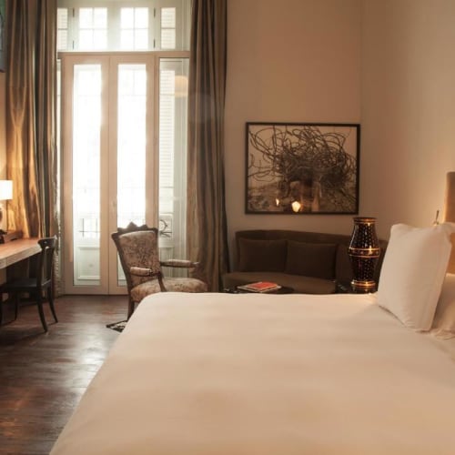 A cozy hotel room with large bed, plush headboard, and a small sitting area near a glass door leading outside.