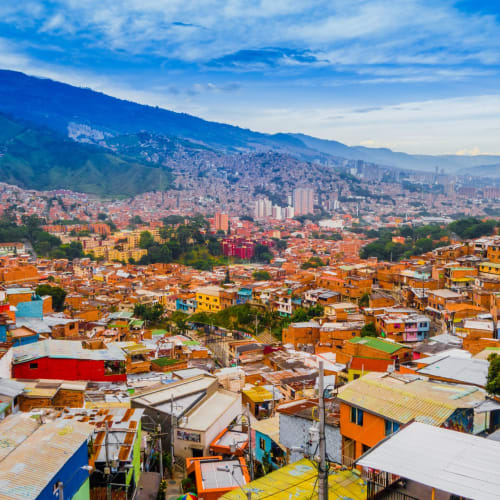 Bunte Häuser und Gebäude prägen den Hang im Stadtteil Comuna 13 in Medellin, Kolumbien, mit Bergen im Hintergrund.
