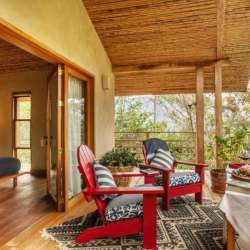 A cozy balcony with two red armchairs and a small table with flowers, overlooking lush green trees.