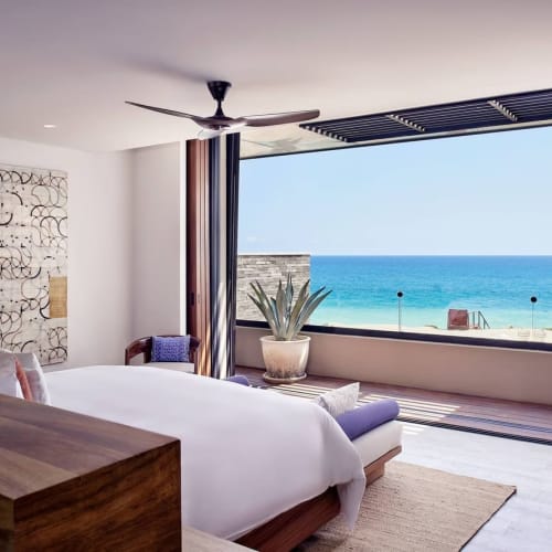 Modern eingerichtetes Schlafzimmer mit großem Bett und freiem Blick auf den Ozean durch ein bodentiefes Fenster in einer Villa.