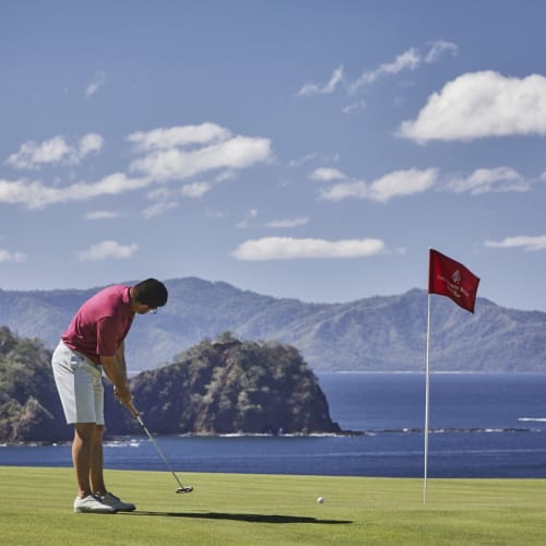 Eine Person spielt Golf auf einem grünen Rasenplatz am Meer unter partly Wolken.
