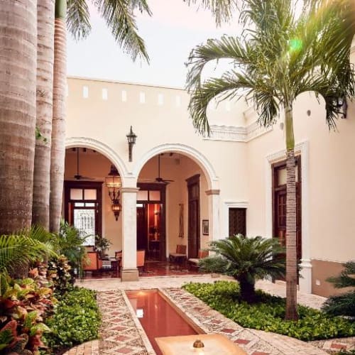 Innenhof des Casa Lecanda Boutique Hotels mit dekorativem Wasserlauf, Palmen und gewölbten Torbögen, die in helle Innenräume führen.