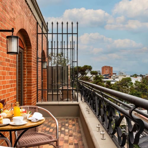 A breakfast setup on a balcony terrace with a view of the city skyline, featuring a table with plates, cups, and condiments against a brick wall.