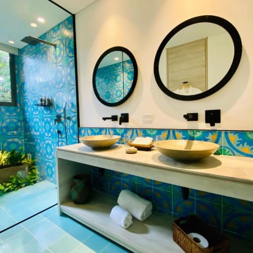 Modern bathroom with two vessel sinks, circular mirrors, and blue patterned tiles on the wall.