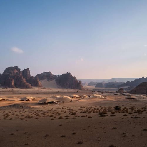 Expansive desert landscape with rocky formations and sparse vegetation under a clear sky.