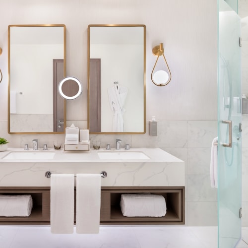Elegantes Badezimmer mit Doppelspiegeln, Wandlampen und einer begehbaren Dusche mit Glastür.