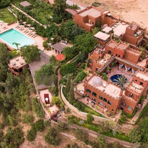 Luftaufnahme einer großen, traditionellen Kasbah mit mehreren Gebäuden, umgeben von Grünfläche und einem nahegelegenen Schwimmbad.
