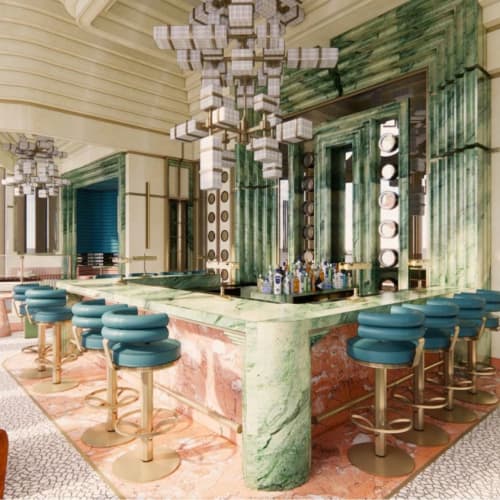 Eine luxuriöse moderne Bar mit grünen Marmorarbeitsplatten und blauen Barhockern in einem schicken Innenraum.