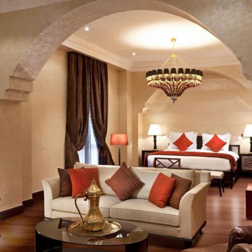 Elegante Suite mit Sitzbereich und Bett, dekoriert mit warmem Licht, dunklen Vorhängen und luxuriösem Mobiliar.