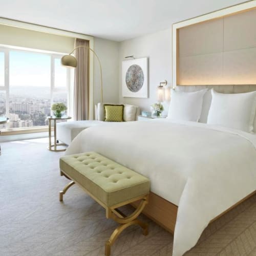 Luxuriöses Deluxe-Hotelzimmer mit großem Bett, Sitzecke und Stadtblick vom Fenster.