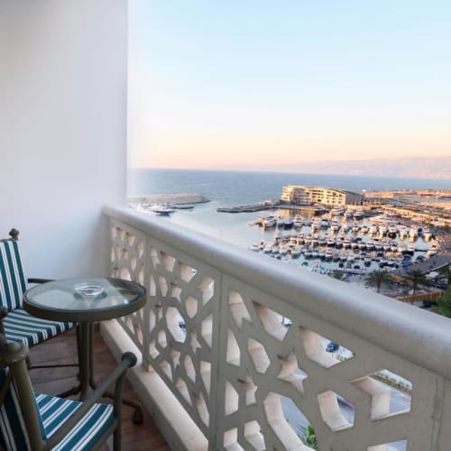 A balcony with two striped chairs and a small round table overlooking a marina and cityscape in Beirut at sunset.