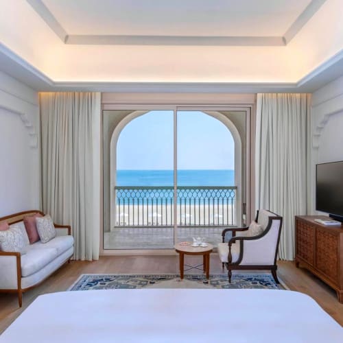 Elegantes Hotelzimmer mit großem Fenster, das zu einem Balkon mit Blick auf den Ozean führt.