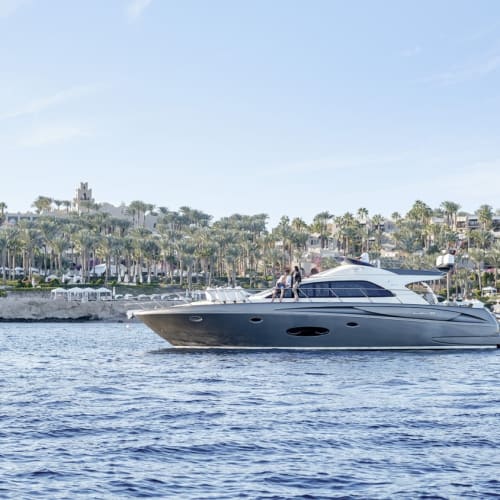 Eine Luxusyacht fährt auf ruhigem Wasser mit einem Resort und Palmen im Hintergrund.