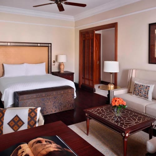 A luxurious hotel suite with a large bed, sitting area, and elegant furniture in a well-lit room.