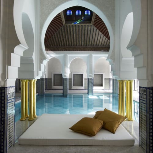 Luxuriöse Innenpoolbereich mit kunstvollen architektonischen Details und einem gepolsterten Lounge-Bett mit Kissen.