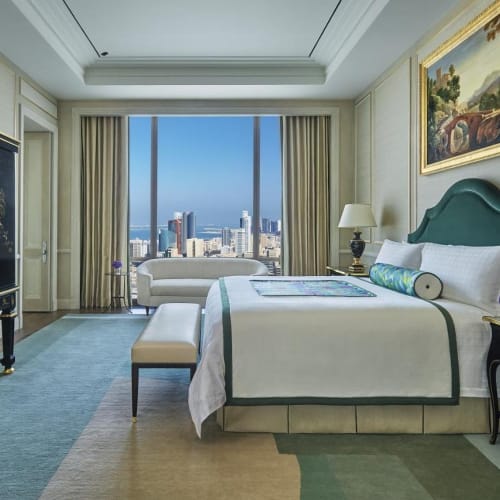 Luxurious hotel room with a large window offering a city view, elegant furniture, and artwork.