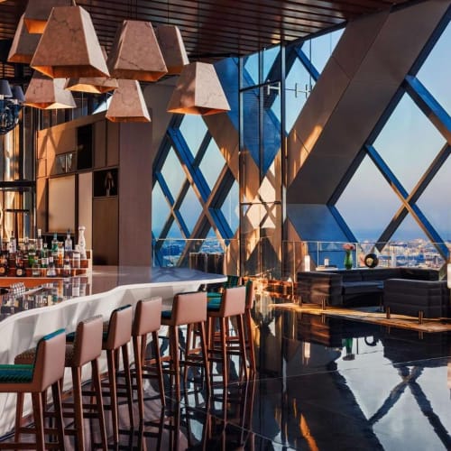 Ein modernes Bar- und Lounge-Bereich in einem Hochhaus mit großen Glasfenstern und Stadtblick.