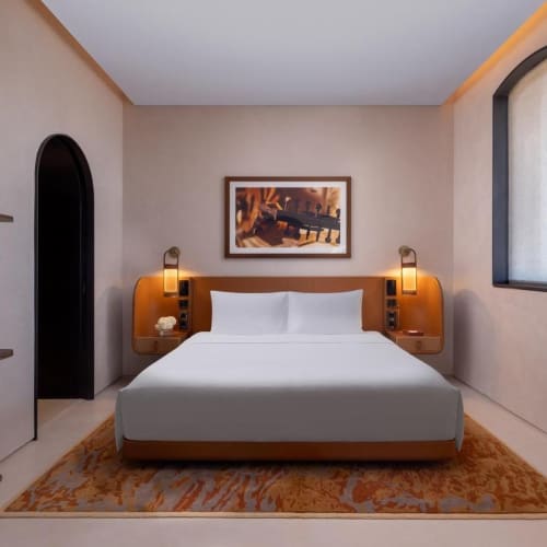 A modern hotel bedroom with a large bed, orange headboard, framed artwork, and soft lighting in a stylish setting.