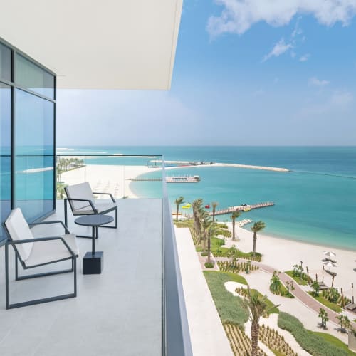 Luxushotel Balkon mit Blick auf einen Strand mit Sonnenliegen und Sonnenschirmen am türkisfarbenen Meer.