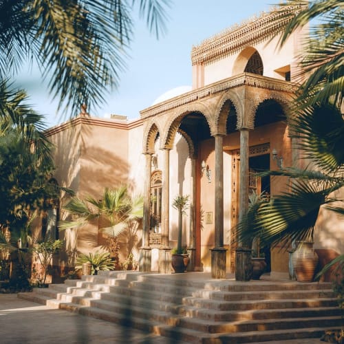 Eleganter Eingang des Al Moudira Hotels mit traditionellen mittelöstlichen Bogen und umgeben von üppigem Grün.