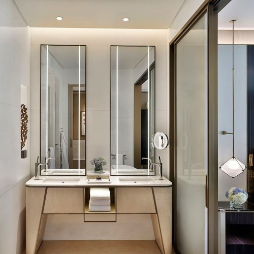 Elegantes Badezimmer mit zwei Spiegeln über einem modernen Waschtisch mit zwei Waschbecken, neben einem Schlafzimmer mit Bett und Wandkunst.