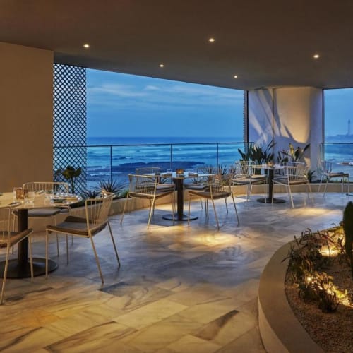 Elegantes Restaurant mit großen Fenstern mit Blick auf den Ozean, eingerichtet mit Tischen und Stühlen zum Essen.
