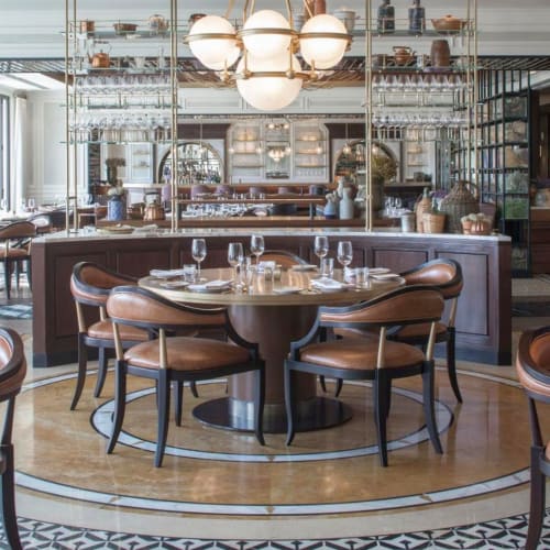 Elegantes Restaurant mit rundem Esstisch, der für eine Mahlzeit gedeckt ist, umgeben von stilvollen Stühlen und anspruchsvoller Innenarchitektur.