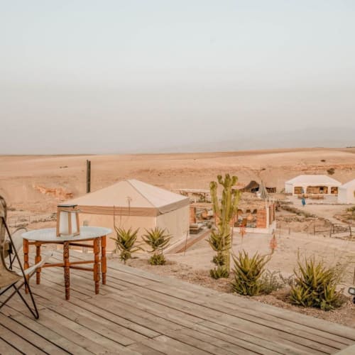 A view from a wooden terrace with chairs overlooking a desert landscape with tents and sparse vegetation at Inara Camp, Agafay.