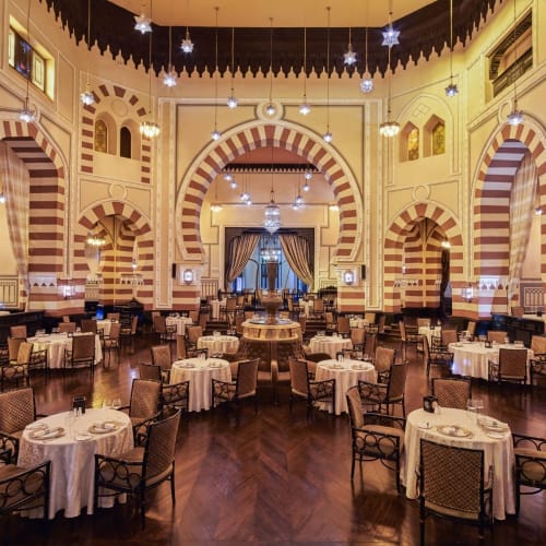 Elegantes Restaurantinnere mit hohen Decken, bogigen Türen und runden Tischen mit weißen Tischtüchern.