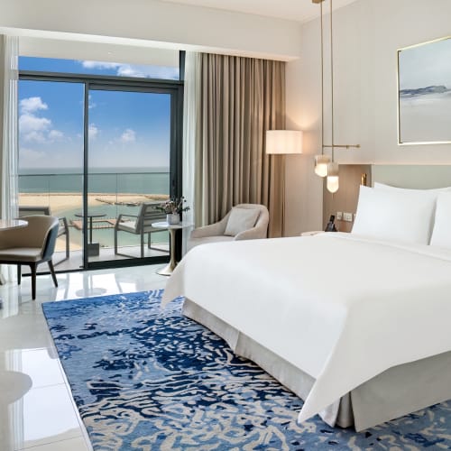 Luxushotelzimmer mit großem Bett, Sitzecke und Balkonblick auf Strand und Ozean.