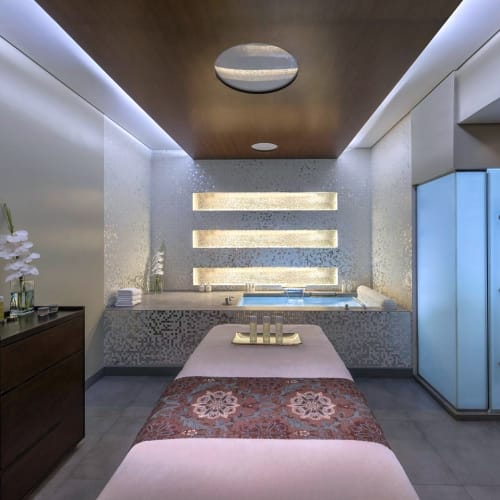 Ein modern gestalteter Wellnessraum mit Massagebett, einem Wasserbereich am Ende und einer lichtdurchfluteten Wand mit horizontalen Lichtleisten.