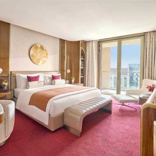 Luxuriöses Hotelzimmer mit Kingsize-Bett, Sitzecke mit Sessel, großem Fenster mit Stadtblick und stimmungsvoller Beleuchtung.