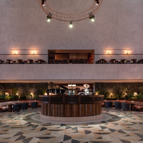 Geräumiges Atrium im The Ned Doha mit einer zentralen runden Bühne mit Musikinstrumenten, Sitzbereichen mit Sesseln und Sofas sowie warmer Umgebungsbeleuchtung.