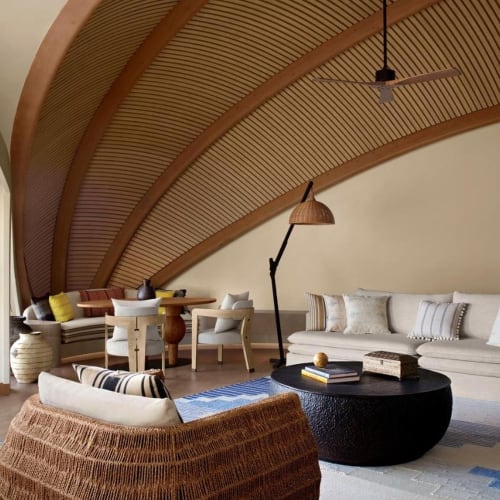 Gemütliches Wohnzimmer mit einer gebogenen Holzdecke, weißen Sofas, einem schwarzen runden Couchtisch und einem Korbatmstuhl.