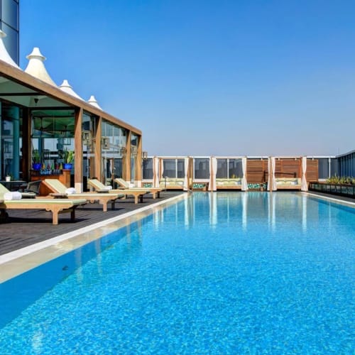 A luxurious hotel rooftop pool with lounge chairs and a clear blue sky.