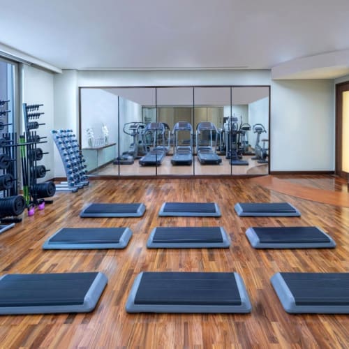 Ein modernes Fitnessstudio mit Holzboden, Spiegel an den Wänden, Trainingsmatten auf dem Boden und verschiedenen Hanteln und Gewichten auf Ständern.