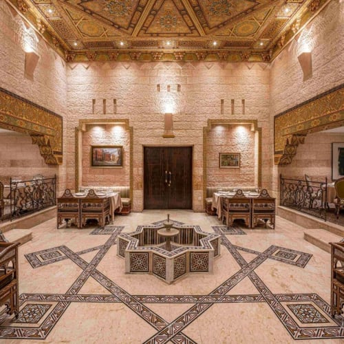 Elegantes Restaurantinterieur mit aufwendig gestaltetem Decke, eingerahmter Kunstwerke und symmetrischer Sitzordnung um einen dekorativen Brunnen.
