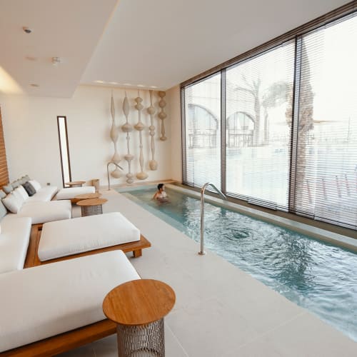 A person relaxing in a small indoor pool at a spa, with large windows showing an outdoor view.