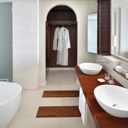 Modernes Badezimmer mit freistehender weißer Badewanne, doppelten Aufsatzwaschbecken auf einer Holzarbeitsplatte und einer Nische mit hängenden weißen Bademänteln.