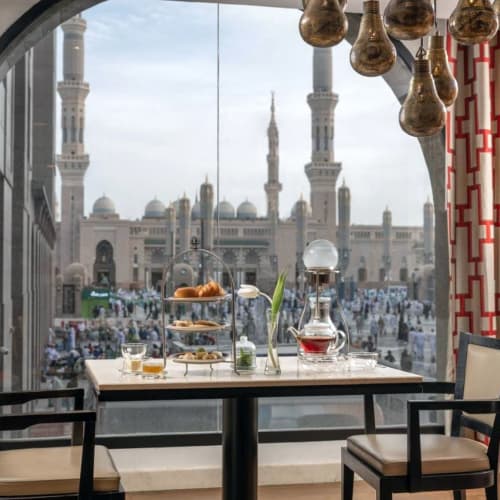 Ein Frühstückstisch mit Snacks und Getränken vor einem großen Fenster mit Blick auf eine Moschee in Madinah.