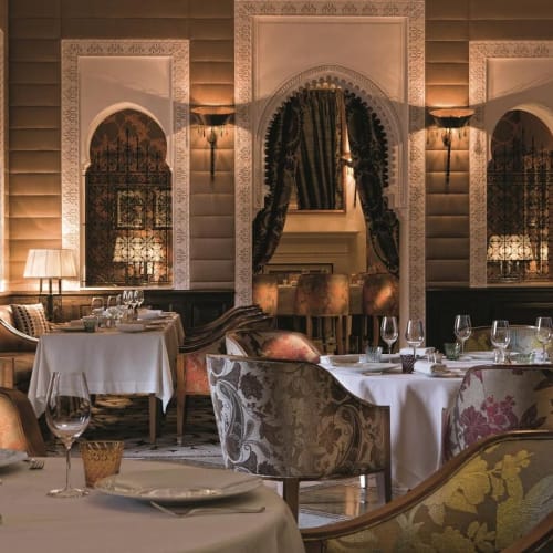 Luxuriöses Restaurant-Innenraum mit eleganten Tischen, kunstvollen Stühlen und marokkanischem Dekor, einschließlich Bögen und Vorhängen.