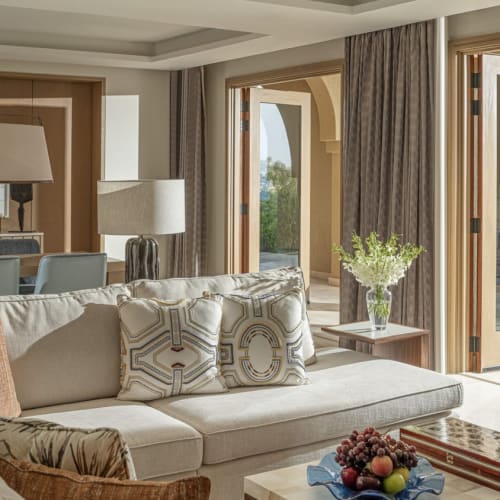 Luxuriöses Wohnzimmer mit offener Terrassentür, die zu einem Pool und einem sonnigen Außenbereich führt, dekoriert mit Kissen und Pflanzen.
