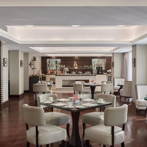 Elegant restaurant in a hotel with white chairs and dark wooden tables, sunlight streaming through large windows.