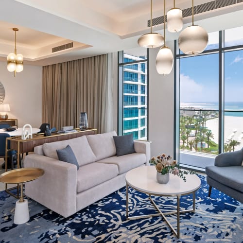 Luxuriöses Wohnzimmer mit großen Fenstern, die einen Blick auf den Strand und den Ozean bieten, mit moderner Einrichtung und Dekor.