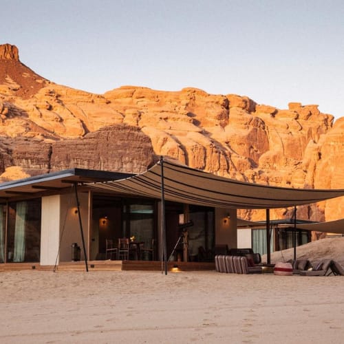 Eine moderne Villa mit großen Glasfenstern in einer Wüstenlandschaft mit roten Felsen und Klippen in AlUla.